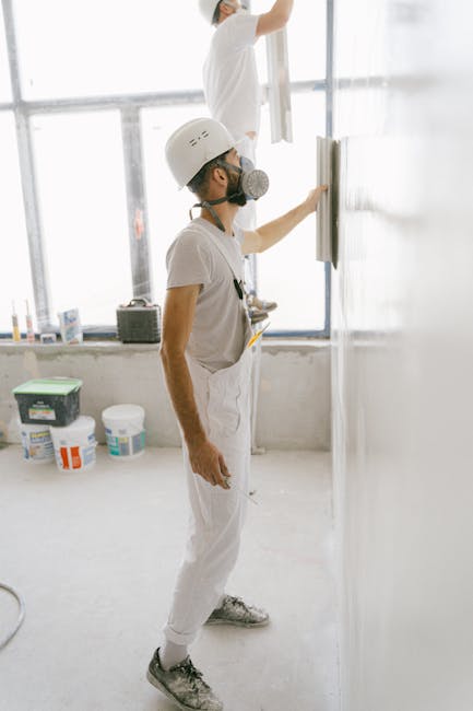 Construction workers wear protective gear while plastering a wall indoors during home renovation.